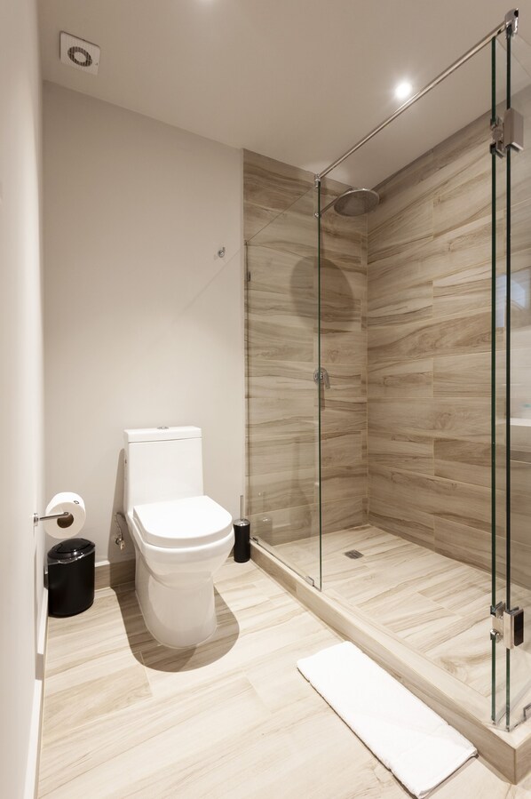 A modern bathroom with a glass-enclosed shower, a toilet, and a white sink.