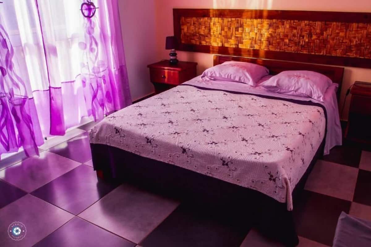 Ein Schlafzimmer mit einem großen Bett, zwei Nachttischen, einem gewobenen Kopfteil und einem Schachbrettfußboden.