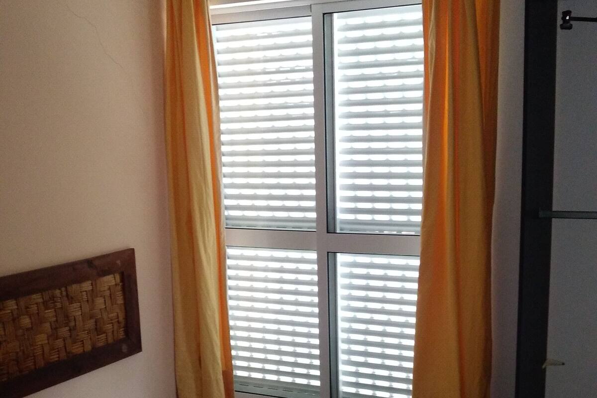Ein Schlafzimmer mit Bett, Vorhängen, einem Fenster und einer Tür.