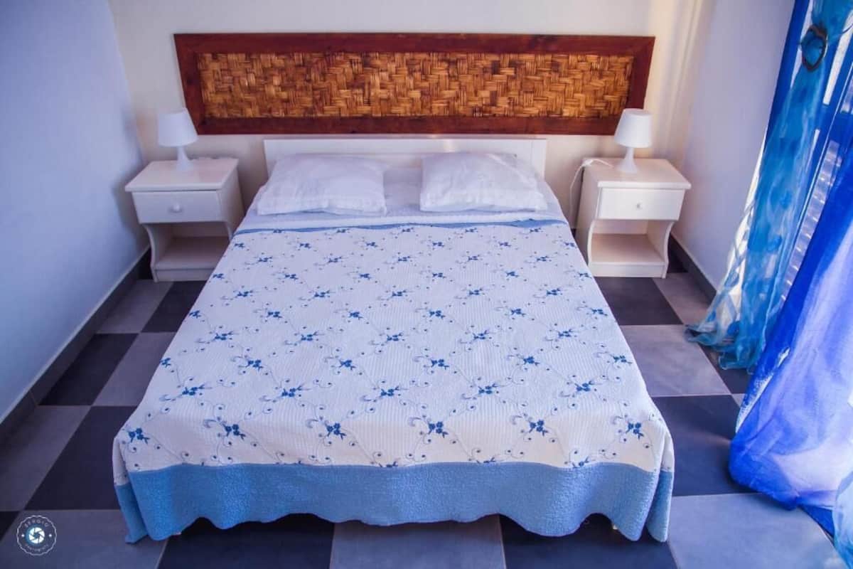 Ein Bett mit einem gewobenen Kopfteil, zwei Nachttischen und einem Schachbrettmuster Boden.