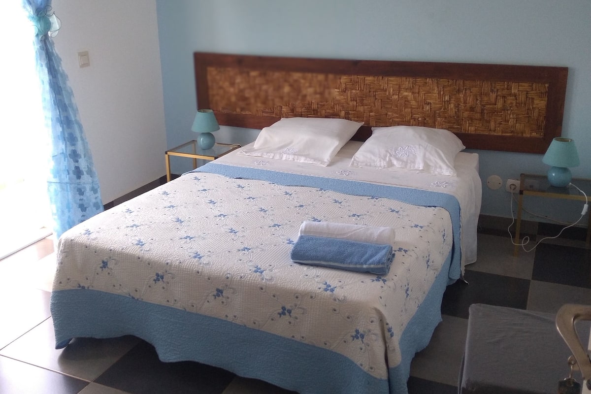 Ein Schlafzimmer mit Schachbrettfußboden, einem Bett mit blau-weißer Bettdecke, zwei Nachttischlampen und einem hölzernen Kopfteil.