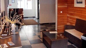 Ein Empfangsbereich mit einer Rezeption, einer Sitzecke mit Sofa und kleinem Tisch sowie einer Zimmerpflanze.