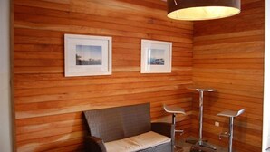 Ein Zimmer mit Holzwandverkleidung, zwei gerahmten Bildern, einem Korbssessel und zwei modernen Stehlampen.