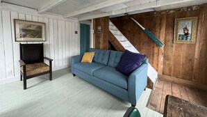 A room with a blue sofa, a wooden chair, a staircase, and a framed picture on the wall. - Oceanside Artists Cottage, Dunfield, Trinity Bay (Dunfield)