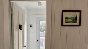 A hallway with white walls and a door leading to a room. There is a framed picture on the wall and a doormat at the entrance. - Oceanside Artists Cottage, Dunfield, Trinity Bay (Dunfield)