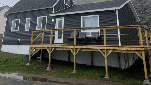 A two-story house with a dark exterior, a front deck, and a small porch area. - Oceanside Artists Cottage, Dunfield, Trinity Bay (Dunfield)