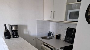 Een functionele keuken met een vaatwasser, een magnetron, een koffiezetapparaat en een spoelbak.