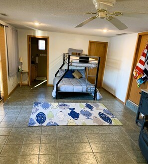 Una habitación con una cama litera, ventilador de techo, alfombra estampada y una puerta que da a otra habitación.