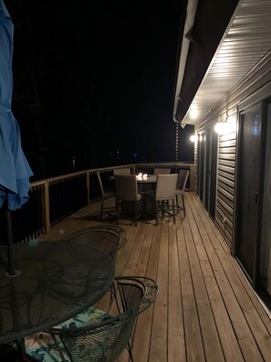 Una terraza de madera con una mesa, sillas, un pozo de fuego y una zona de estar cubierta.