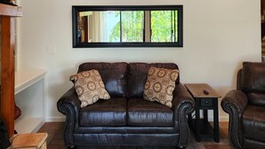 A living room with a leather sofa, a wooden railing, and a view of the outdoors.