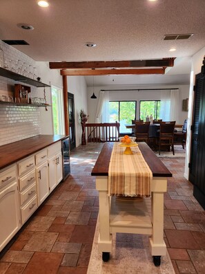 Una cocina con encimera de madera, armarios blancos y una zona de comedor con mesa y sillas.