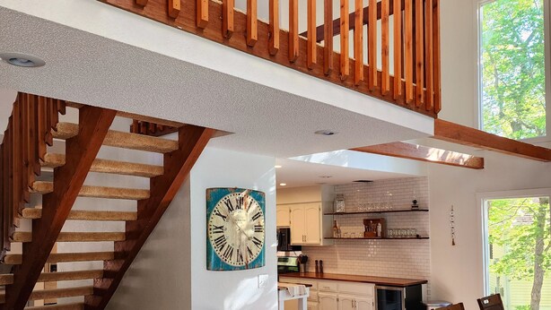 A spacious kitchen with a large window, a wooden staircase, and a clock on the wall.