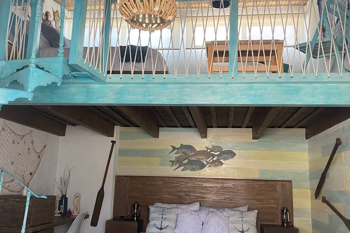 Un dormitorio con cama alta, cabecera de madera, lámpara colgante y un mural en la pared.