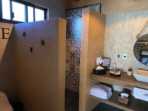 A bathroom with a wooden partition, a mirror, a sink with toiletries, and patterned tiles.