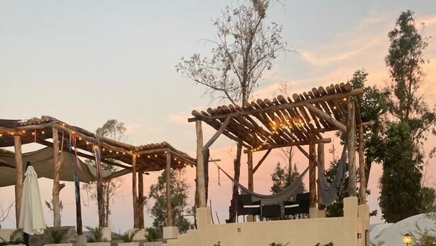 Una pareja en un jacuzzi, con una pérgola de madera y sillones de descanso al fondo.