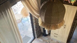 Una escalera de caracol con barandilla de hierro forjado que conduce a una habitación con un ventanal grande, una lámpara de mimbre y un armario de madera.