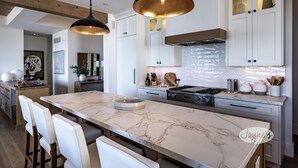 Une cuisine moderne avec des meubles blancs, un îlot en marbre, des luminaires suspendus et une cuisinière en acier inoxydable.