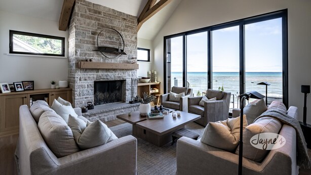 Un salon spacieux avec une cheminée en pierre, de grandes fenêtres donnant sur la mer et un mobilier moderne.