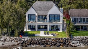 Une grande maison moderne à deux étages, dotée d’une façade en pierre, de grandes fenêtres et d’un mur de soutènement en pierre à l’avant.
