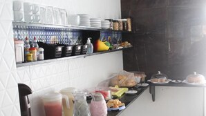 En buffetopsætning med forskellige retter og drikkevarer på en buffetvogn, omgivet af hylder med køkkenudstyr og beholdere.