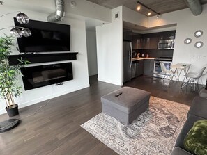 A modern living room with a flat-screen TV, a grey ottoman, and a patterned rug. - Downtown across from arena wifi and laundry (Winnipeg)
