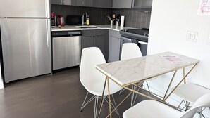 A modern kitchen with stainless steel appliances, a white marble countertop, and a dining area with white chairs and a gold-trimmed table.