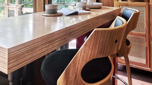 A wooden dining table with chairs, a bookshelf, and a view of trees through large windows. - 1960 Mid-Century Modern Nature Retreat (Cambridge)