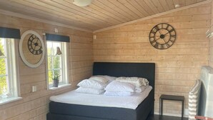 A bedroom with a bed, two wall clocks, a window, a small table, and a chair. - Experience Fjällkroken, an Exquisite Mountain Cabin Built in 2016 (Undersåker)