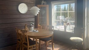 A dining area with a wooden table and chairs, a clock on the wall, and a window with a view of trees. - Experience Fjällkroken, an Exquisite Mountain Cabin Built in 2016 (Undersåker)