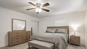 A bedroom with a bed, a nightstand, a bench, a dresser, and a ceiling fan.