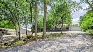 A gravel driveway leading to a building with a garage, surrounded by trees and a grassy area.