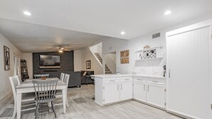 A modern kitchen with white cabinetry, a dining area with a table and chairs, and a staircase leading to another level.