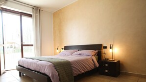 Ein Schlafzimmer mit einem Bett, zwei Nachttischlampen, einem Nachttisch und einer Schiebetür zu einem Balkon.