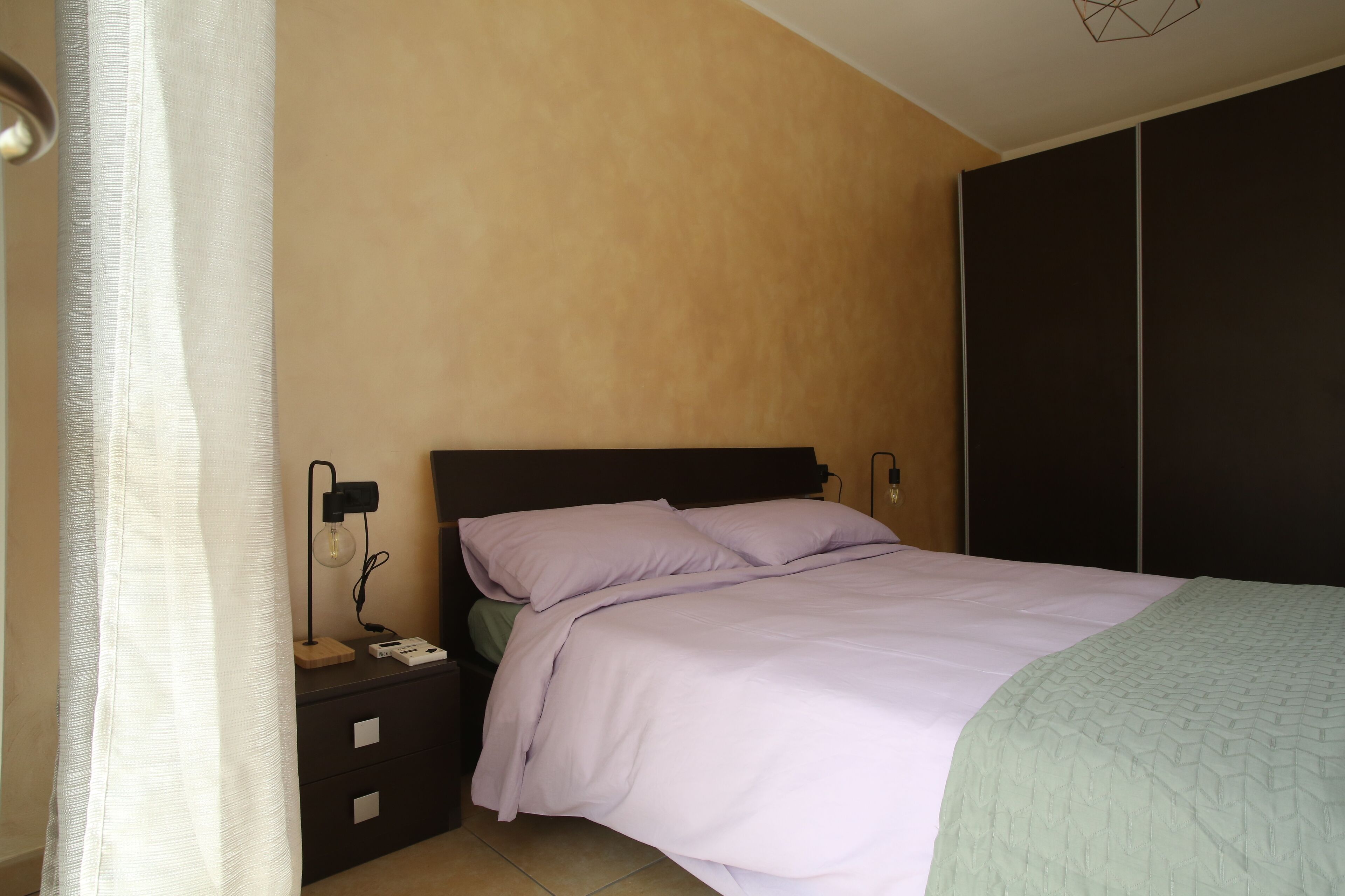 A bedroom with a bed, nightstand, lamp, and wardrobe.