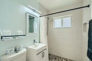 A bathroom with a toilet, sink, and shower. There are two rolls of toilet paper on the toilet, a towel rack above the sink, and a shower curtain rod.