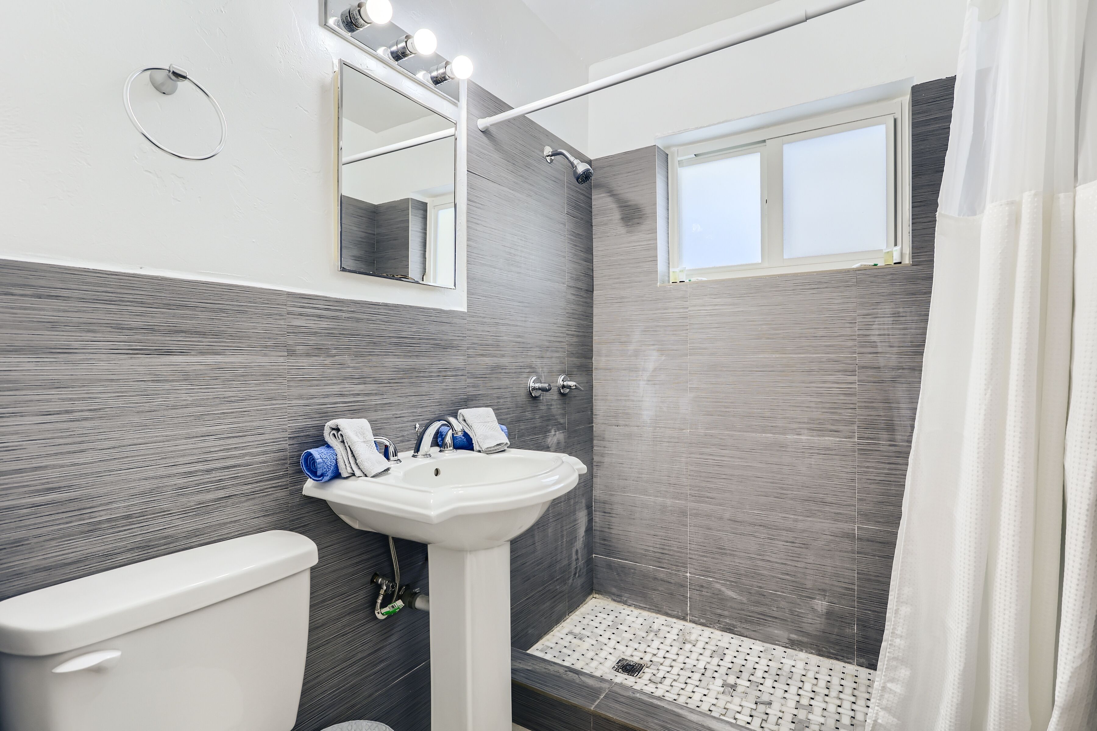 A modern bathroom with a white toilet, a pedestal sink, and a shower.