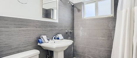 A modern bathroom with a white toilet, a pedestal sink, and a shower.