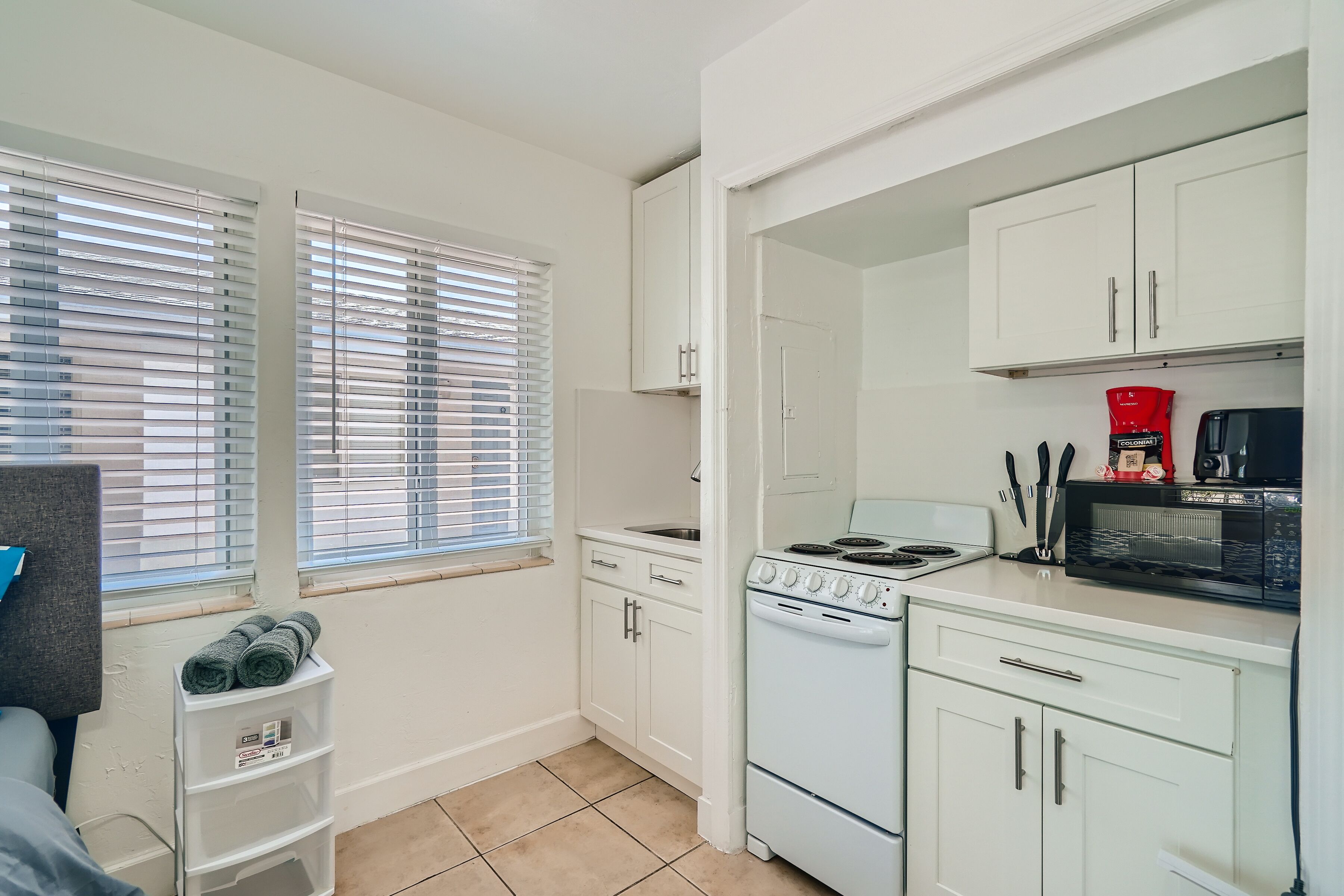 A compact kitchen with white cabinets, a stove, a microwave, and a sink.