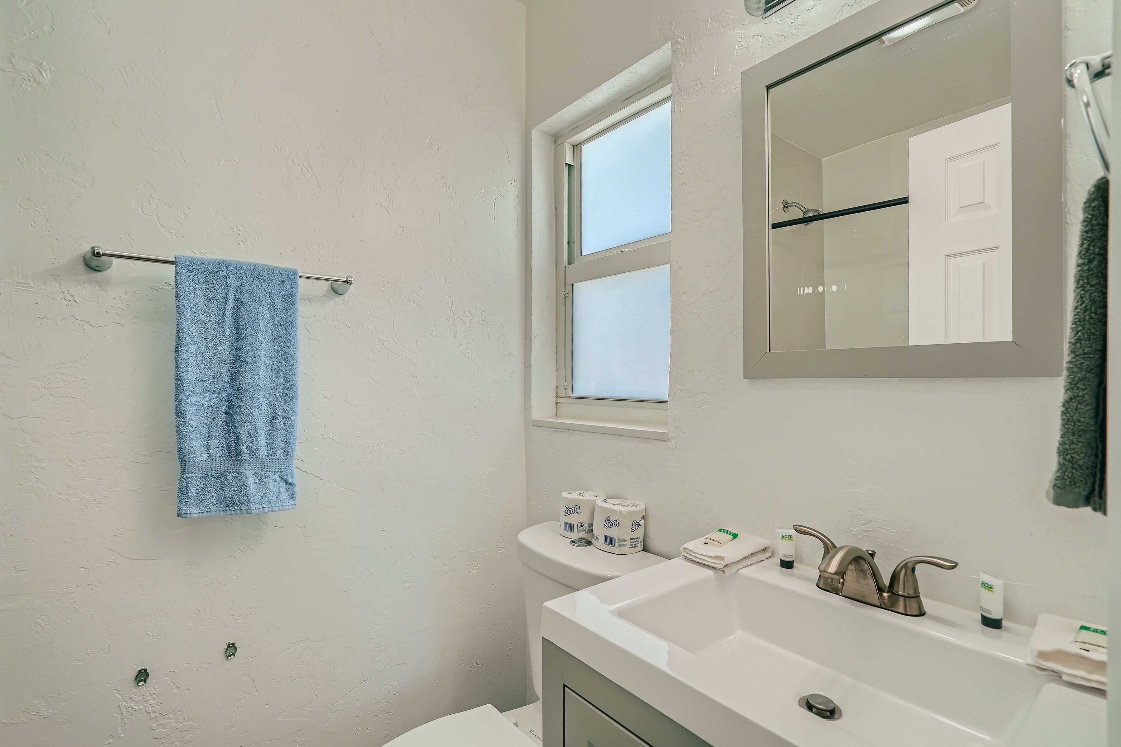 A bathroom with a white sink, a mirror, and a towel rack with a blue towel.