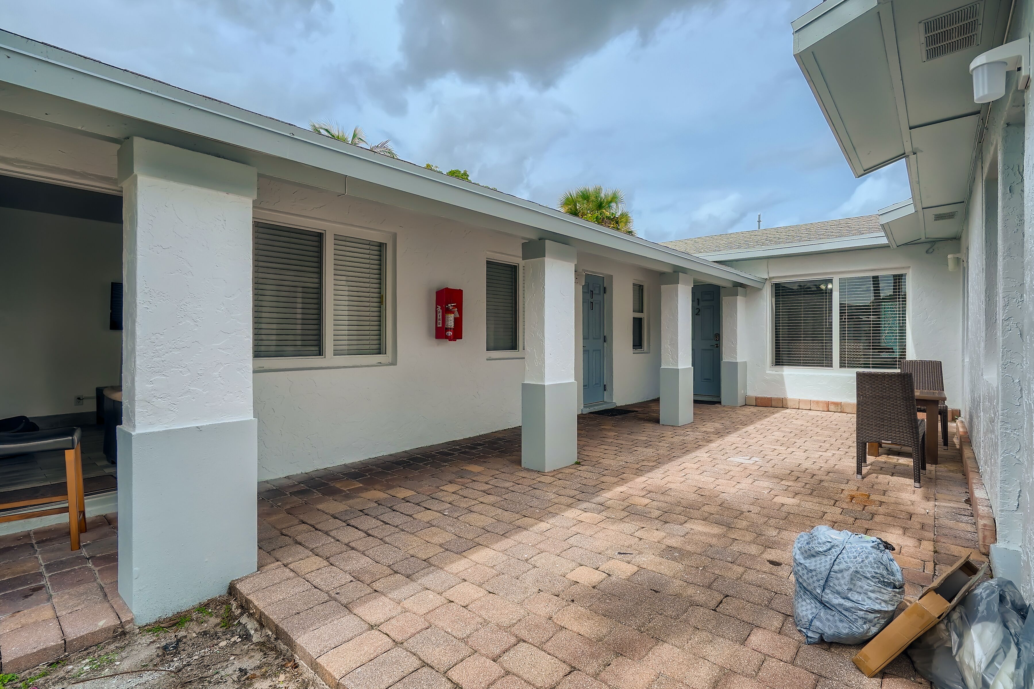A covered outdoor area with a brick floor, white walls, and a red fire extinguisher.