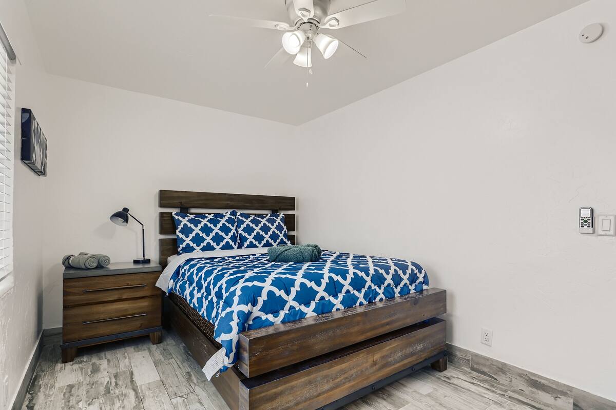 A bedroom with a wooden bed, a nightstand, a ceiling fan, and a wall-mounted light.