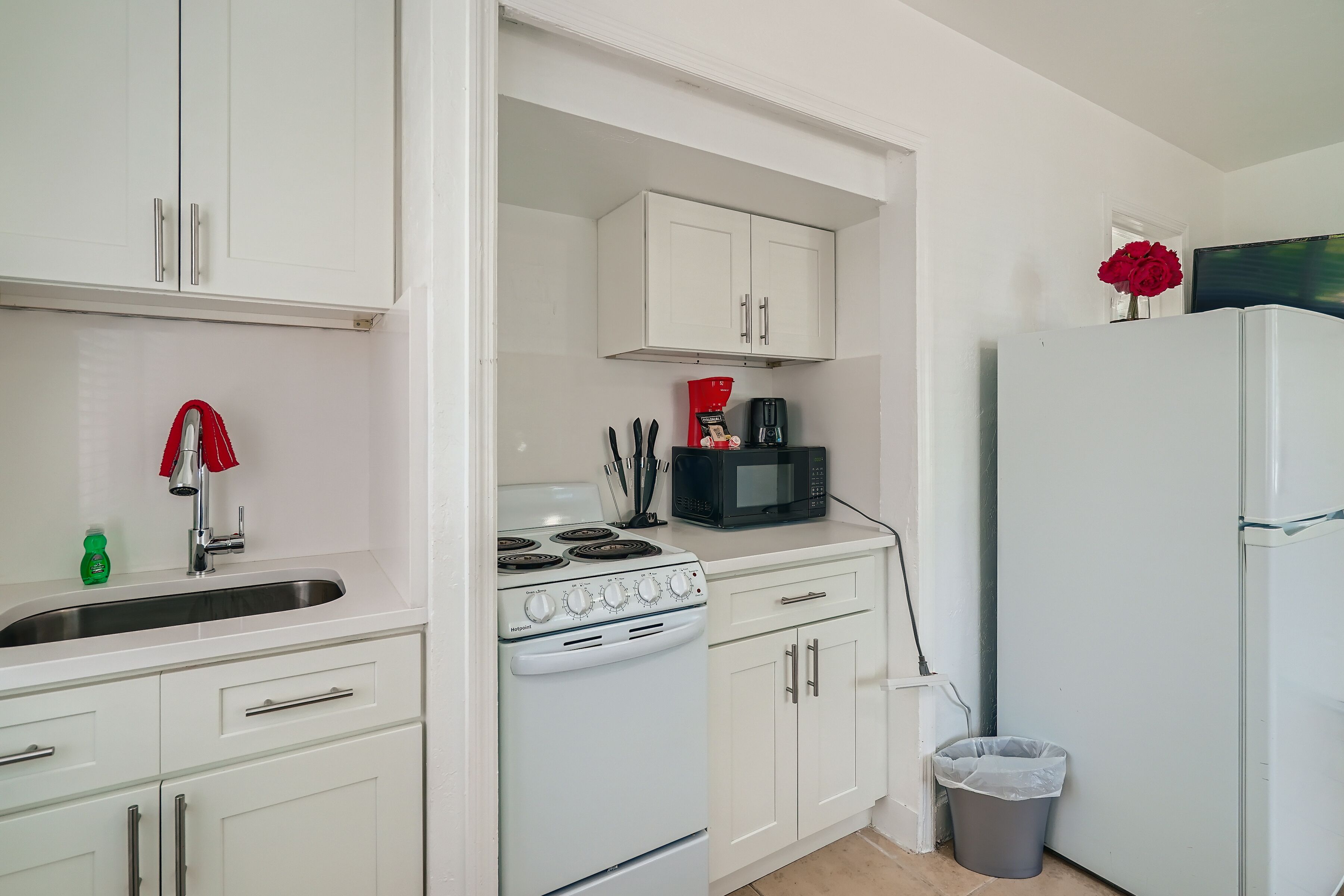 A compact kitchen with white cabinets, a stove, a sink, and a refrigerator.