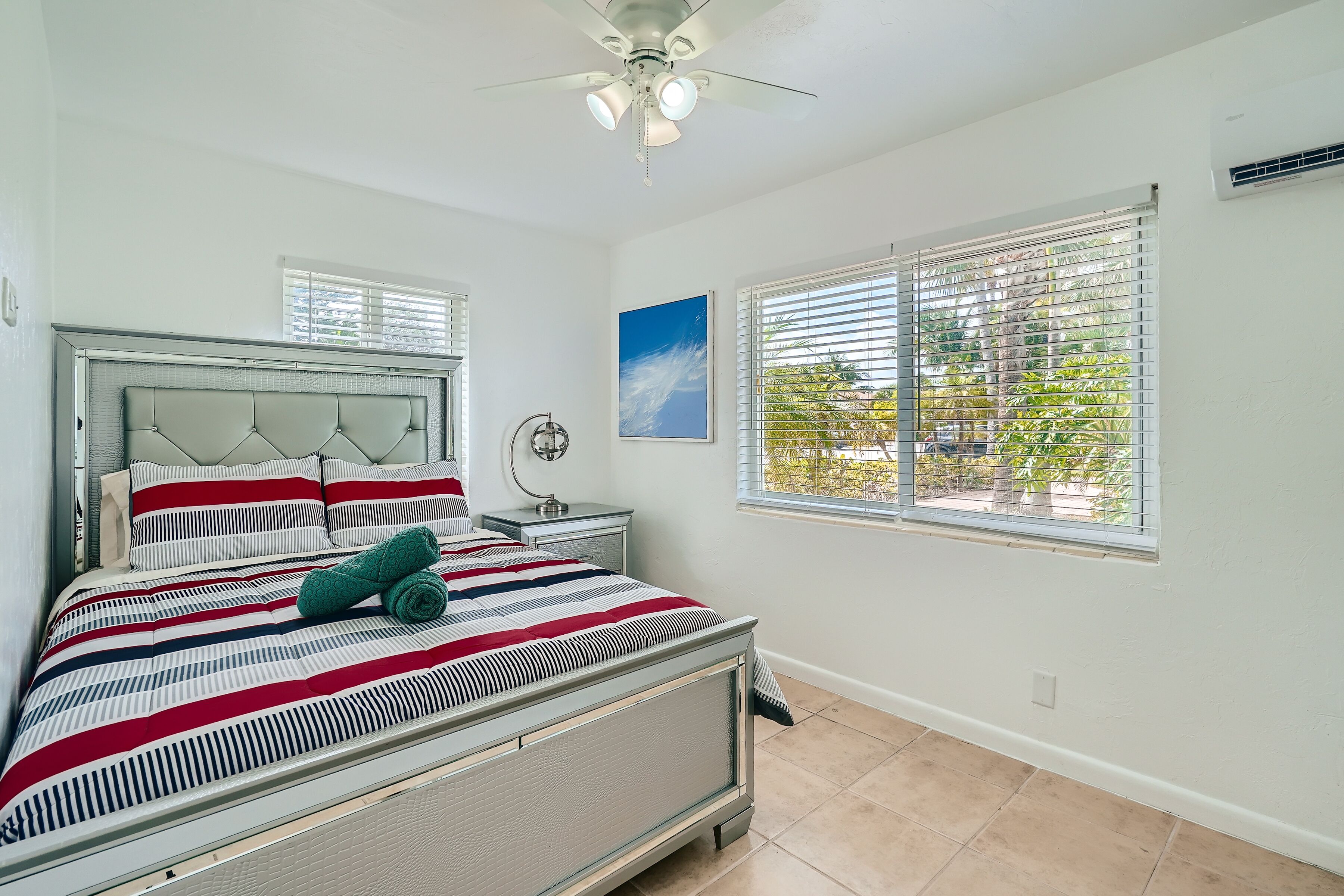 A bedroom with a bed, a ceiling fan, a window with blinds, and a wall-mounted air conditioner.