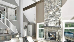 Una sala de estar moderna con chimenea de piedra, un sofá de cuero y una escalera.
