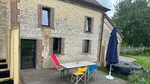 A patio with a table and chairs, a wooden deck, and a brick building. - Joli Gîte de Campagne au Milieu des Champs - 4 à 8 Personnes (Neauphe-sur-Dive)
