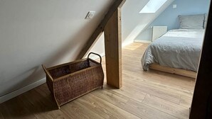 A room with a sloped ceiling, wooden flooring, a bed, and a wicker basket. - Joli Gîte de Campagne au Milieu des Champs - 4 à 8 Personnes (Neauphe-sur-Dive)