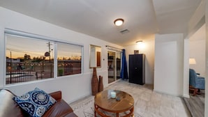Ein modernes Wohnzimmer mit einem Ledersofa, einem Glastisch und Blick auf einen Balkon mit Außenbeleuchtung.