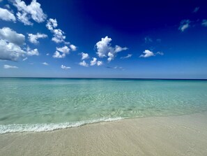 A beach with clear turquoise water and a sandy shore under a blue sky with scattered clouds.