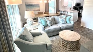 A modern living room with a grey sofa, a round coffee table, and a dining area with a wooden table and chairs. - Beachside Dreams, at Boutique Beachside Villas, Newly Renovated and Decorated (Santa Rosa Beach)