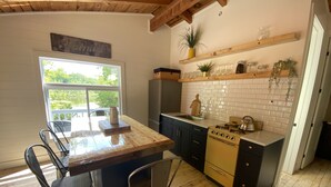 A kitchen with a wooden island, bar stools, a stove, and a window overlooking greenery. - The Bay Stay! Fully Renovated Off-Grid Waterfront Cottage on Burridge Lake  (Godfrey)